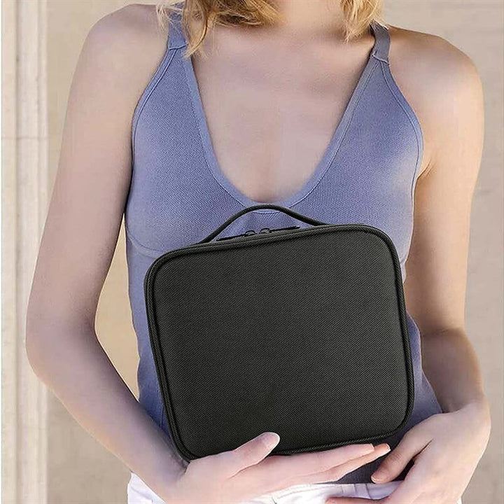 A woman in a sleeveless, light purple top holds the UNIQ makeup travel bag—a black, rectangular cosmetic bag with adjustable compartments and a handle—in front of her torso.